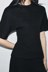 Top de cuello redondo y manga corta, confeccionado en tejido suave con costura central vertical y cintura entallada.
