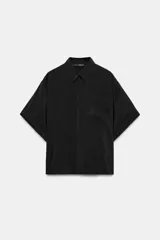 Camisa fluida de manga corta con cuello solapa, bolsillo de plastrón en el delantero y cierre frontal con botones ocultos. Presenta aberturas laterales en el bajo.
