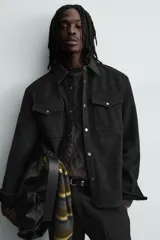 Sobrecamisa de corte relajado confeccionada en tejido efecto piel color marrón oscuro. Presenta cuello solapa, cierre frontal con botones metálicos, mangas largas con puños abotonados y dos bolsillos de plastrón con solapa en el pecho.