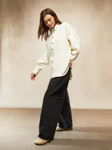 Camisa de pana color crema, con cuello camisero, botones negros en el frente y mangas largas abullonadas con puños.