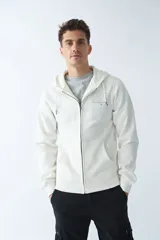 Campera de felpa color blanco hueso, con capucha y cordón ajustable, cierre frontal con cremallera, bolsillos laterales, logo y arte estampado en el pecho.