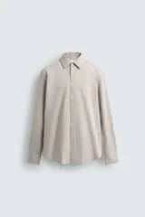 Camisa de corte slim fit confeccionada en tejido de algodón, con estampado de cuadros pequeños en tonos beige y blanco. Presenta cuello italiano, manga larga con puños abotonados y cierre frontal con botones.