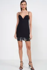 Vestido corto negro con escote corazón y tirantes finos. Presenta una hilera de apliques cuadrados espejados en el ruedo.