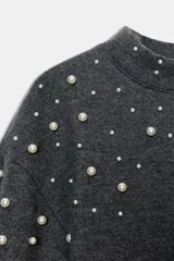 Jersey de cuello perkins y manga larga en color gris oscuro, con detalle de aplicaciones de perlas distribuidas en la parte superior y a lo largo de las mangas.