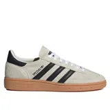 Championes Adidas Handball Spezial de mujer, confeccionados en gamuza color beige con las icónicas tres tiras y el talón en negro, acompañados de una suela de goma marrón translúcida.