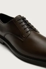 Zapato de vestir tipo derby, color marrón oscuro, con parte superior lisa, horma redonda, cordones y suela con ligero tacón.