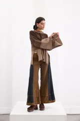 Pantalón de jean estilo wide leg con diseño bicolor en tonos marrón y negro. Presenta paneles laterales oscuros, costuras a la vista en color ocre y bolsillos frontales tipo parche en la parte inferior de las piernas.
