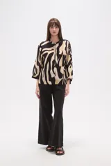 Camisa de corte holgado con estampado animal print tipo cebra en tonos negro y beige. Presenta cuello mao, cierre frontal con botones y un bolsillo aplicado en el pecho.