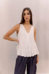 Musculosa blanca de diseño holgado con escote en V, costuras decorativas frontales, tablas encontradas en el centro y un delicado volado en el ruedo.