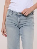 Jean wide leg de tiro medio, color azul claro, confeccionado en denim de algodón con un toque de elastano. Cuenta con cinco bolsillos, presillas para cinturón y cierre frontal con botón. El diseño destaca por su pretina regulable con cruce y broches metálicos.
