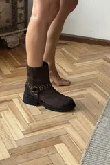 Bota corta de cuero marrón, con suela track negra y diseño de caña media. Cuenta con una tira con tachas y hebilla metálica alrededor del tobillo.