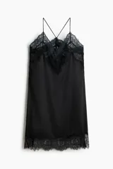Vestido corto lencero de satén negro, con escote en V pronunciado y ribetes de encaje floral en el escote y el bajo. Cuenta con finos tirantes spaghetti cruzados en la espalda.