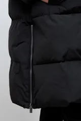 Campera puffer larga de color negro, con diseño capitoneado, capucha integrada y cierre frontal oculto. Presenta cierres laterales en el ruedo para mayor comodidad.