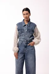 Campera de jean negra con mangas largas tejidas en crochet con diseño calado y detalles florales en relieve. Presenta cuello camisero, cierre frontal y bolsillos en el pecho.