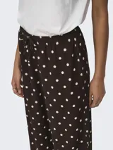 Pantalón suelto color marrón con estampado de lunares blancos, tiro medio y cintura elástica con cordón de ajuste.