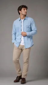 Camisa de jean de corte clásico, color celeste claro, con cuello italiano, cierre frontal de botones oscuros y dos bolsillos frontales con solapa.