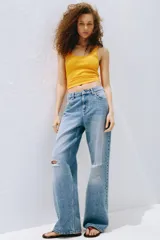 Jean de tiro alto confeccionado en denim de algodón lavado con diseño de cinco bolsillos, piernas rectas y holgadas, y detalles de roturas en las rodillas.