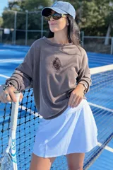 Remera de manga larga en tejido acanalado color marrón, con diseño holgado y escudo bordado en el centro del pecho.