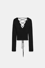 Top de punto ajustado de color negro, de manga larga y escote en V. Cuenta con la espalda descubierta con tirantes finos cruzados y cordón ajustable en el bajo.