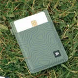 Billetera vertical de cuero genuino en color verde militar con bolsillo elástico estampado con patrón topográfico. Incluye protección RFID y argolla lateral.