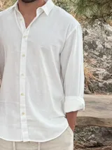 Camisa blanca de lino, de manga larga con puños doblados, cuello clásico y botones frontales.