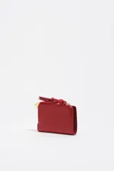 Billetera pequeña de estructura rígida, color negro, con estampado frontal en color dorado con la palabra "BIMBA". Posee cierre superior con tirador de tela amarillo mostaza.