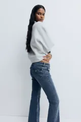 Jean de denim elástico color azul con efecto deslavado, tiro bajo, corte ajustado hasta la rodilla y diseño acampanado. Cuenta con cierre de botón y cremallera, bolsillos delanteros y bolsillos traseros con solapa y botón.