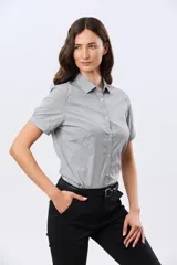 Camisa celeste rayada de manga corta, con cuello camisero y cierre frontal con botones. Presenta un corte entallado y un pequeño detalle de placa metálica en el borde inferior.