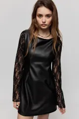 Vestido corto de símil cuero negro, de corte recto, escote amplio y sin mangas, combinado con mangas largas de encaje negro.