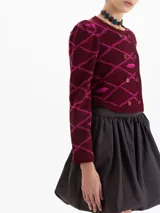 Saco tipo cardigan corto tejido en jacquard con diseño gráfico de labios y cadenas. Presenta cuello redondo, mangas largas con hombros ligeramente abullonados y cierre frontal con botones.