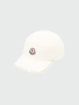 Gorra de baseball color blanco crudo, con visera curva y costuras decorativas en zigzag a contratono en el borde. Presenta un parche circular bordado con el logo de la marca en el frente.