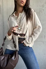 Camisa de corte holgado en color beige, con cuello clásico, cierre frontal de botones y mangas largas que presentan un delicado bordado tonal en los antebrazos.