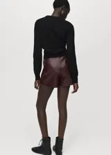 Falda pantalón corta de efecto piel en color bordó, de tiro medio y diseño cruzado con cierre de cremallera lateral.