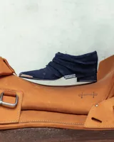 Botineta de gamuza azul marino con diseño drapeado, punta fina con puntera metálica y placa metálica decorativa en el lateral. Posee taco bajo cuadrado.