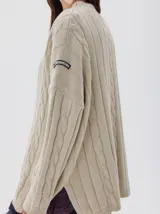 Buzo tejido de punto color beige, con cuello subido, diseño oversized y aberturas laterales en el ruedo.