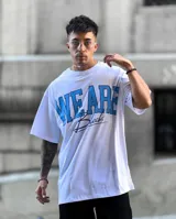 Remera oversize blanca de manga corta con estampado frontal "WE ARE" en color celeste y texto cursiva en negro.