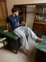 Pantalón de jogging gris melange de corte baggy, confeccionado en algodón. Presenta cintura elástica con cordón largo ajustable, bordado decorativo en la pierna izquierda y botones metálicos en la parte inferior de la botamanga para ajustar el ancho.