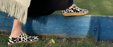 Zapatillas bajas con estampado animal print de vaca en blanco y negro, con cordones marrones y suela color caramelo.