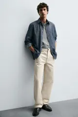 Pantalón chino de algodón color beige claro, corte recto, con cierre frontal de cremallera y botón, bolsillos delanteros y bolsillos traseros de doble vivo con botón.