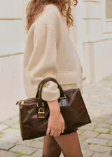 Chaqueta de corte recto y diseño medio, confeccionada en tejido bouclé color beige. Presenta cuello alto, manga larga, cierre frontal oculto con cremallera y botones a presión, y dos bolsillos de parche laterales.