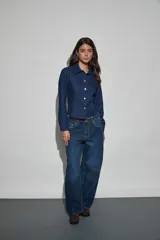 Campera corta de denim azul oscuro con cuello camisero, mangas largas y cierre frontal de botones metálicos dorados.