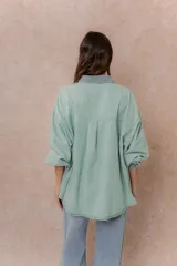 Camisa lila de calce relajado y manga larga, con cuello clásico, puños y bolsillo delantero en denim contrastante. Cierre frontal con broches metálicos.