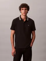 Chomba de piqué Calvin Klein color negro, con cuello clásico y ribetes a rayas blancas, cartera de dos botones y pequeño monograma CK bordado en el pecho.