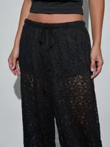 Pantalón negro de encaje con transparencias, tiro medio y cintura elástica ajustable con cordón.