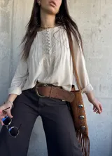 Blusa beige de corte oversize, con mangas largas, botones forrados en el frente y detalles de puntillas y alforzas verticales.