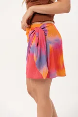 Minifalda multicolor con estampado abstracto en tonos naranja, rosa y violeta. Diseño cruzado con lazo lateral.