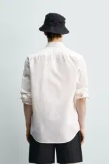 Camisa de corte relajado color celeste, confeccionada en mezcla de algodón y seda. Presenta cuello solapa, cierre frontal de botones, manga larga con puños abotonados y dos bolsillos de plastrón con solapa en el pecho.