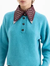Sweater de punto color azul, con cuello camisero de cuero en contraste con detalles de tachas metálicas y cierre frontal con botones. Presenta mangas largas con puños acanalados y un corte holgado.