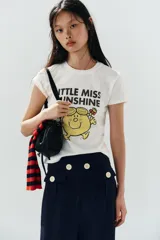 Camiseta de algodón flamé color blanco, de corte regular con cuello redondo y manga corta. Presenta un estampado frontal con texto y gráfico del personaje Little Miss Sunshine.
