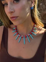 Collar corto con cuentas de cerámica rojas, pinchos de piedra reconstituida turquesa, cristales checos y mostacillas. Se cierra con cadena de acero quirúrgico para regular el largo.